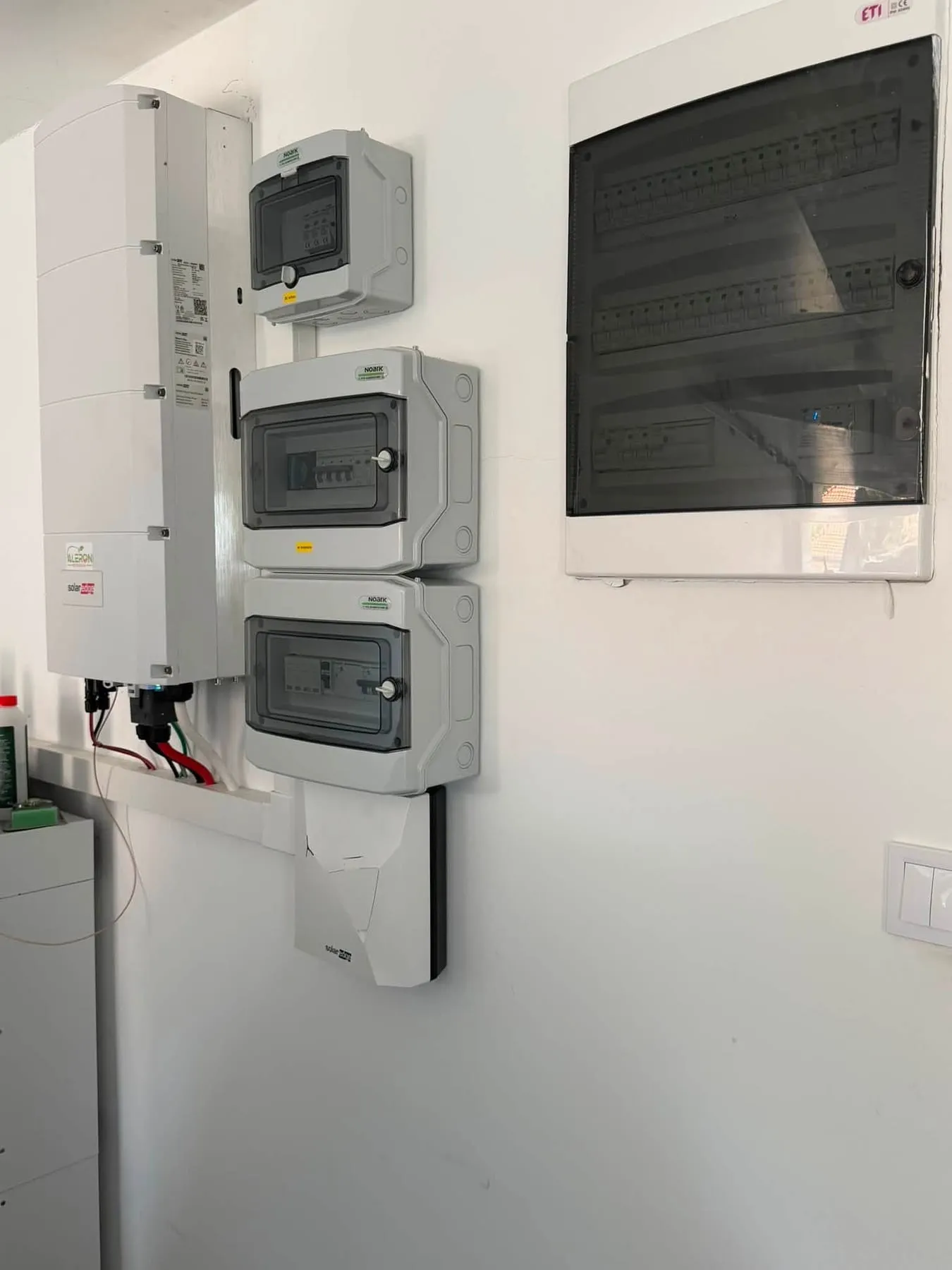 Falra szerelt inverter mellett AC és DC oldali védelmi szekrények, tőlük jobbra zárt ajtós lakáselosztó tábla